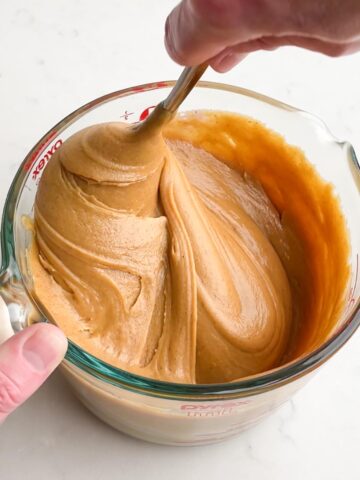 Hand stirring the melted peanut butter fudge mixture in a glass measuring cup. 