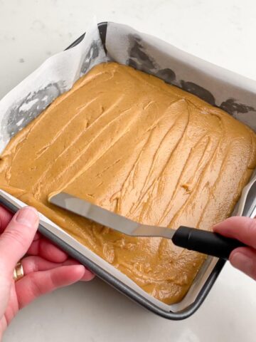Hand spreading peanut butter fudge mixture in square pan. 