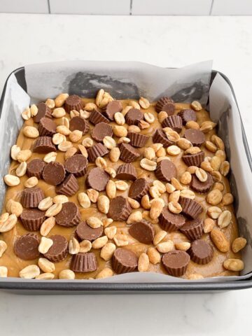 Peanut butter fudge in square pan topped with peanut butter cups and peanuts. 