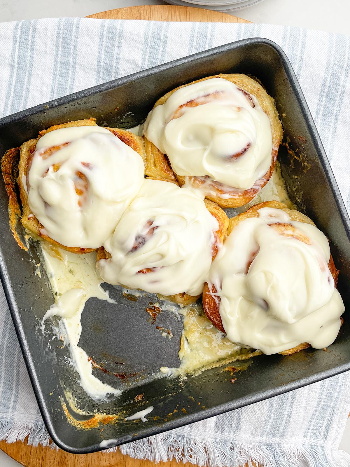 four cinnamon rolls with frosting in a baking pan.