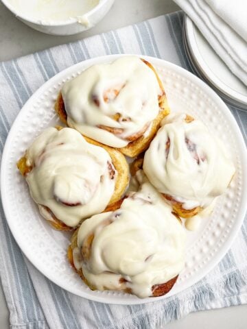 four cinnamon rolls with frosting on a white plate.