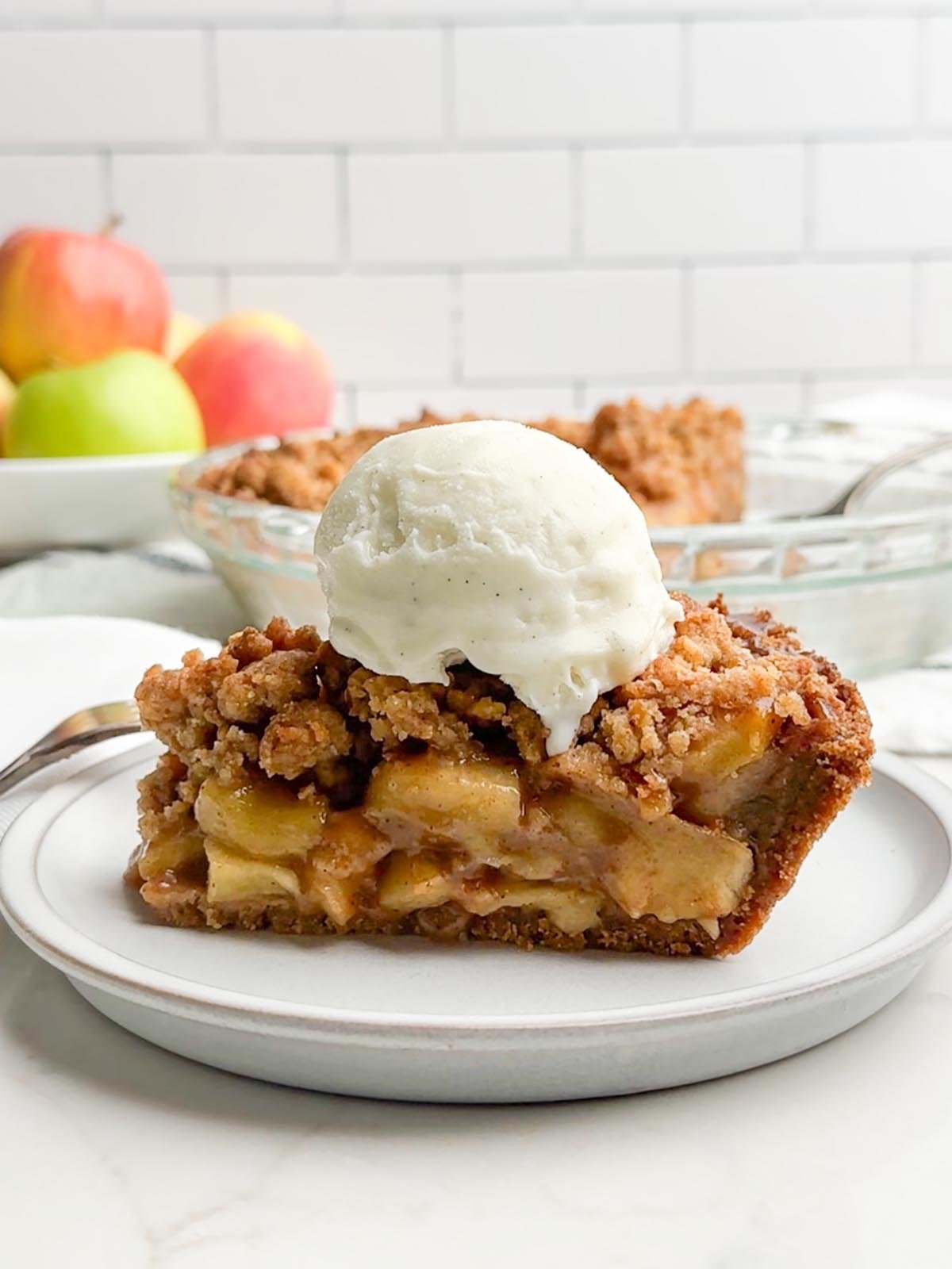 side view of apple pie with graham cracker crust topped with vanilla ice cream.