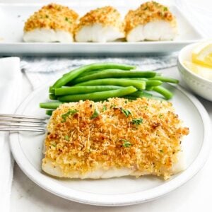 Baked parmesan panko cod on a white plate with green beans