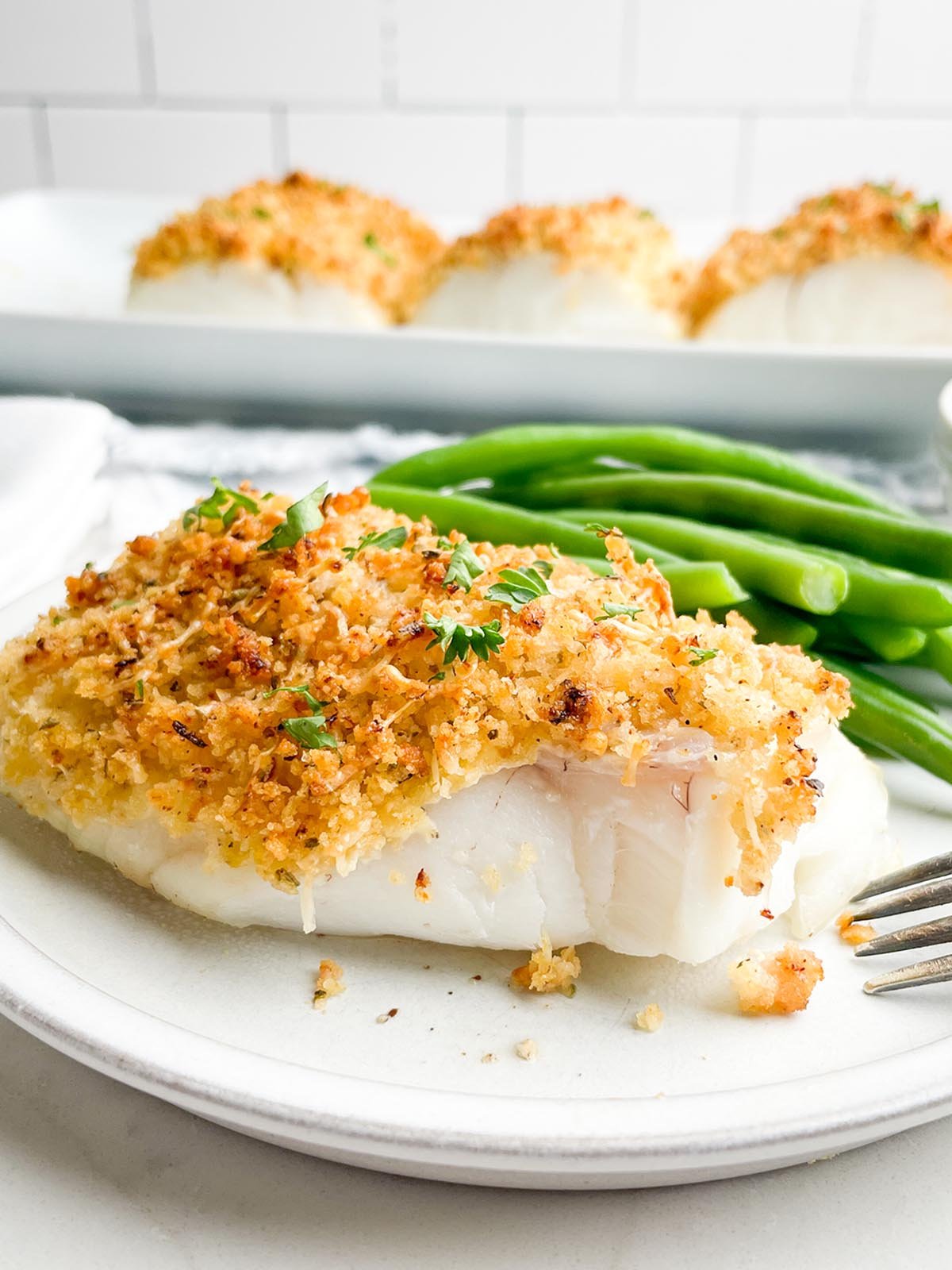 Baked parmesan panko cod on a white plate with green beans