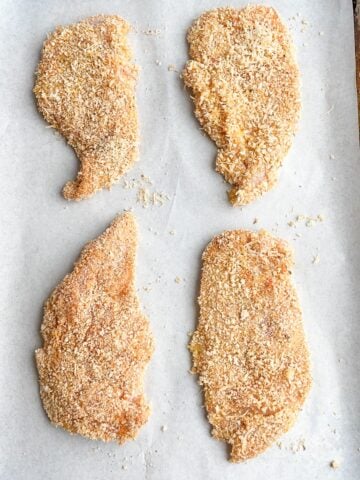 panko thin sliced chicken on parchment lined baking sheet