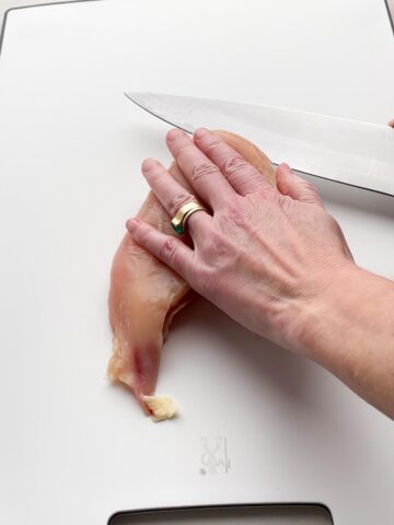 hand holding chicken breast flat and slicing it with a knife