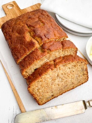 loaf of banana bread with pancake mix on white parchment on wooden cutting board.