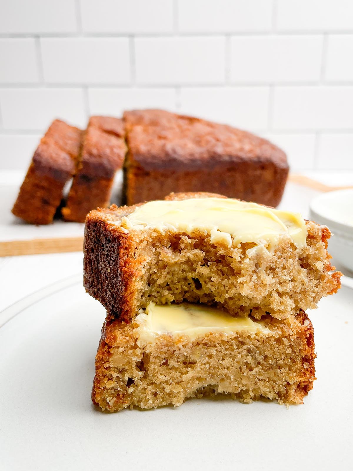 stack of two pieces of banana bread with loaf of banana bread in background.