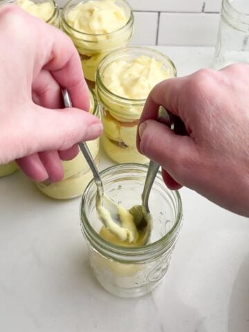 hands spooning pudding into a mason jar. 