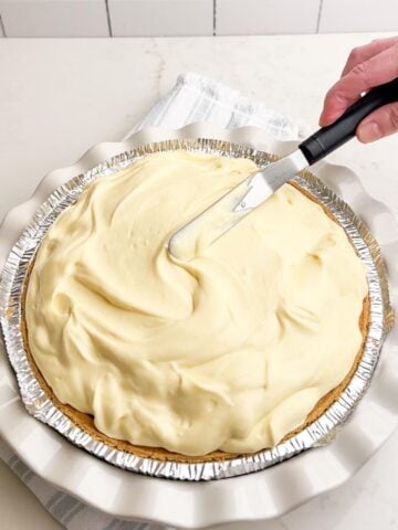 hand holding offset spatula spreading pudding on top of pie.