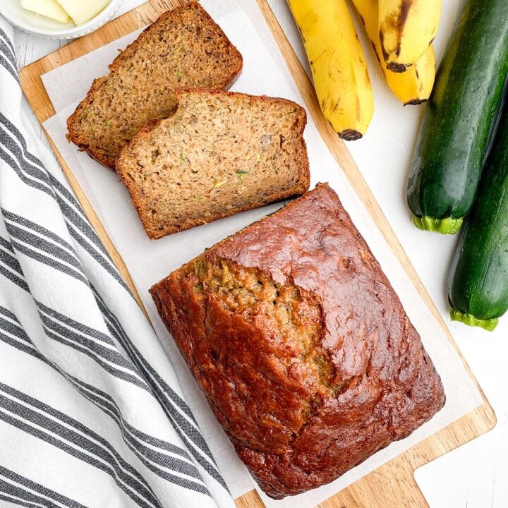 lopartial loaf and 2 pieces of banana zucchini bread on a wooden cutting board
