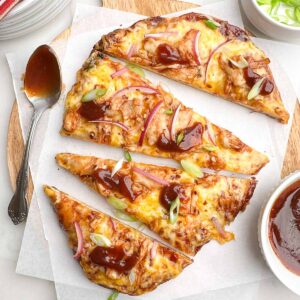 bbq chicken flatbread cut into slices on parchment covered wooden cutting board