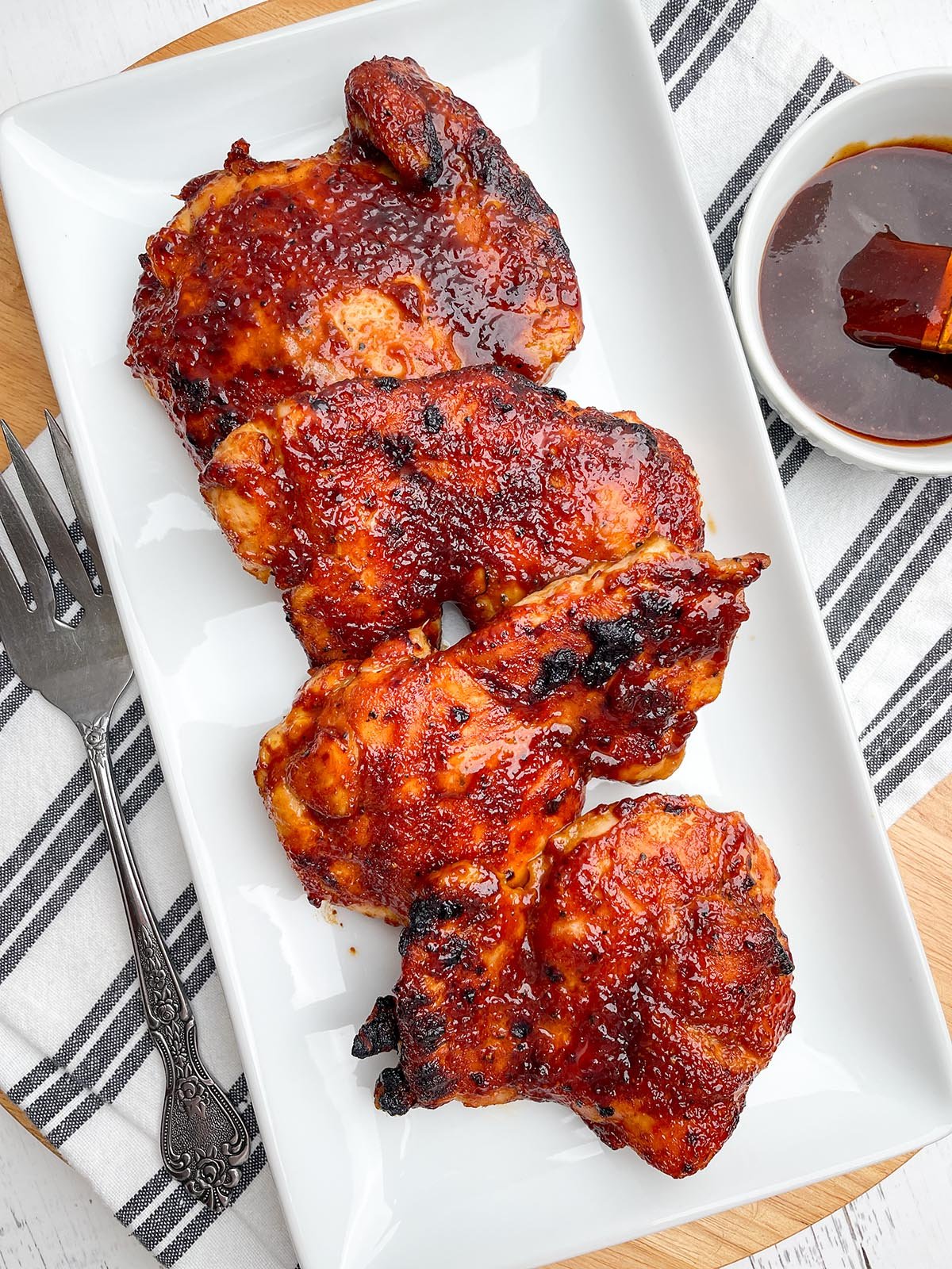 air fryer bbq chicken thighs on a white platter next to bowl of bbq sauce