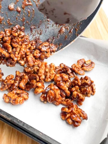 spatula sliding brown sugar candied walnuts onto parchment paper.