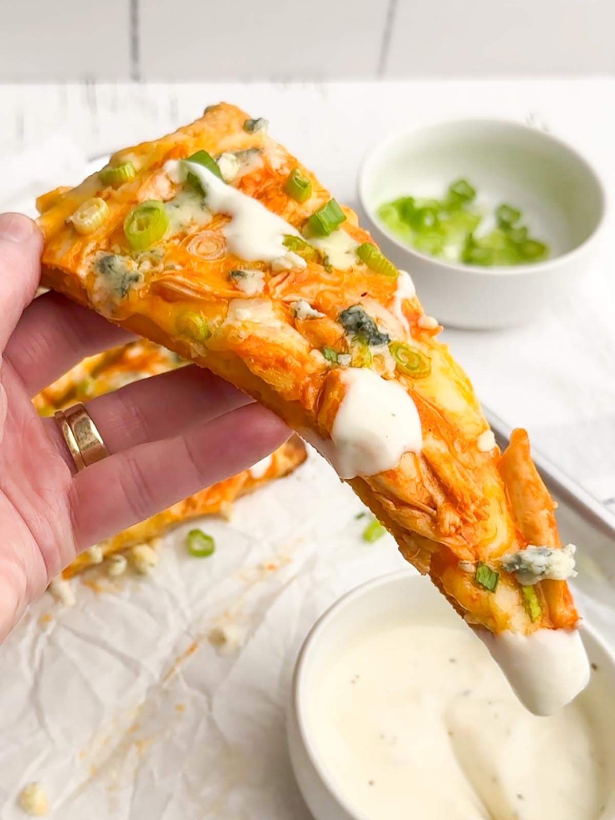 hand holding up a slice of buffalo chicken flatbread