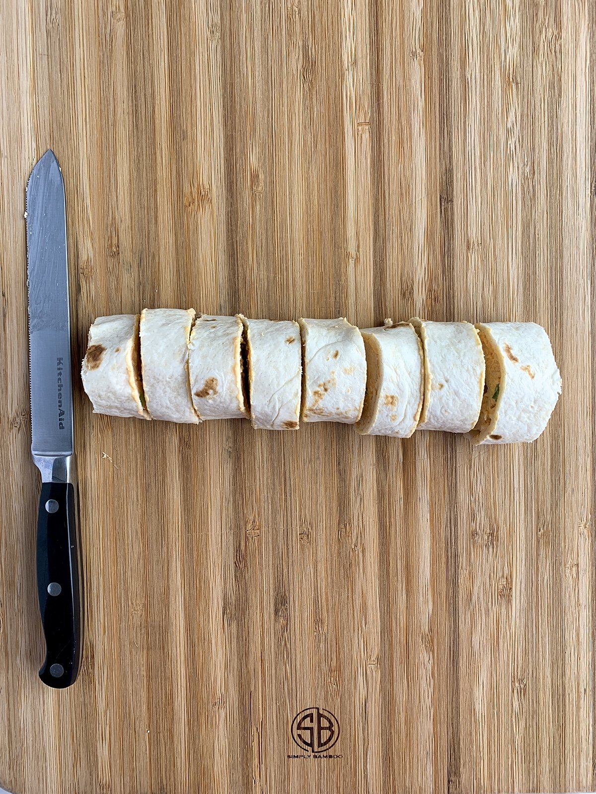 Buffalo Chicken Pinwheel tortilla cut up into 8 pieces on a wooden cutting board with a serrated knife