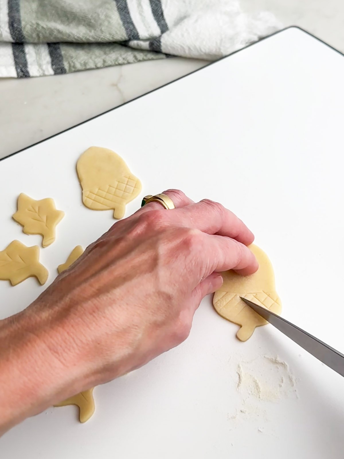 Hand holding a knife detail onto pie dough cutouts.