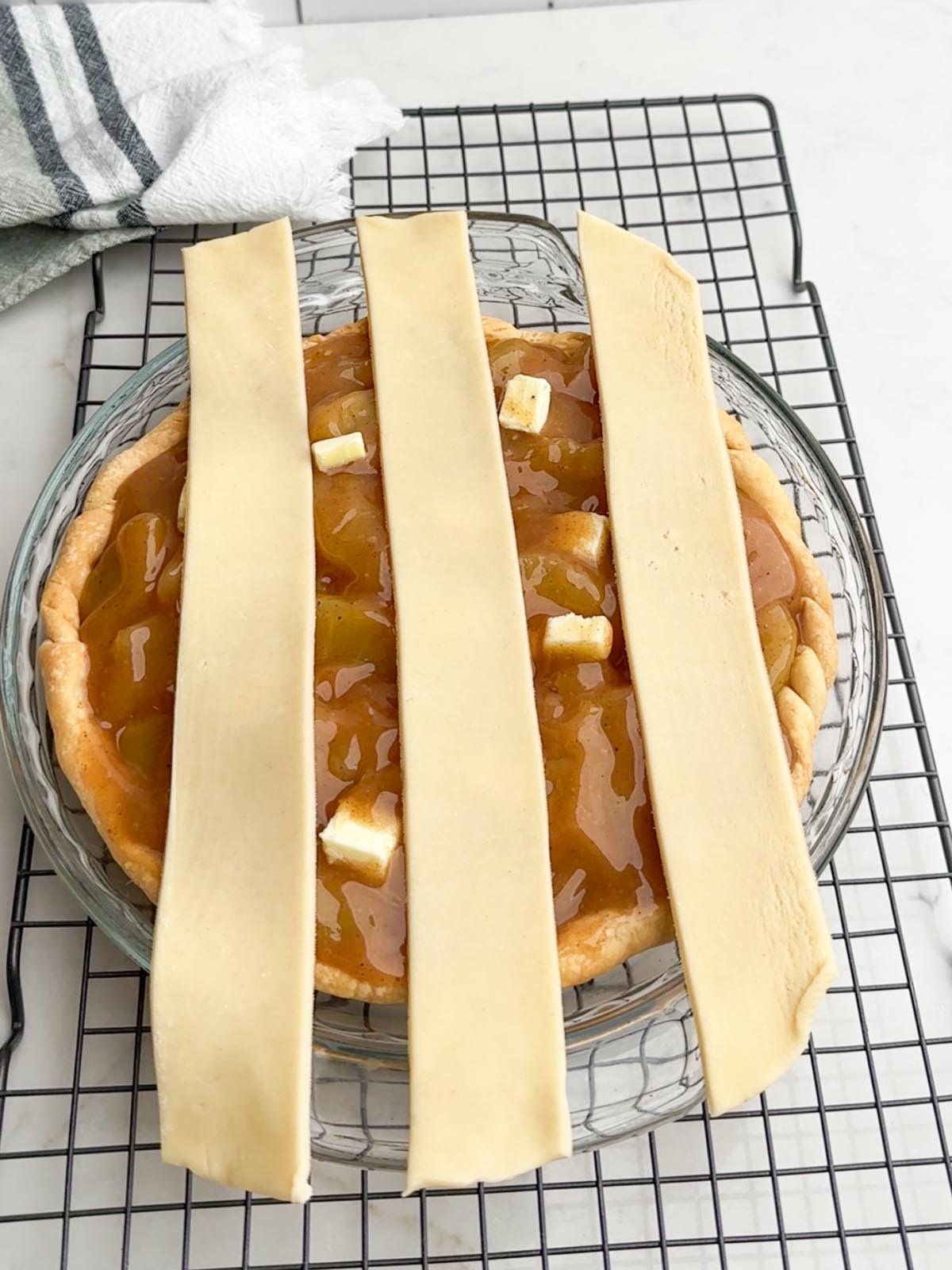 Three strips of pie dough placed vertically on top of apple pie.