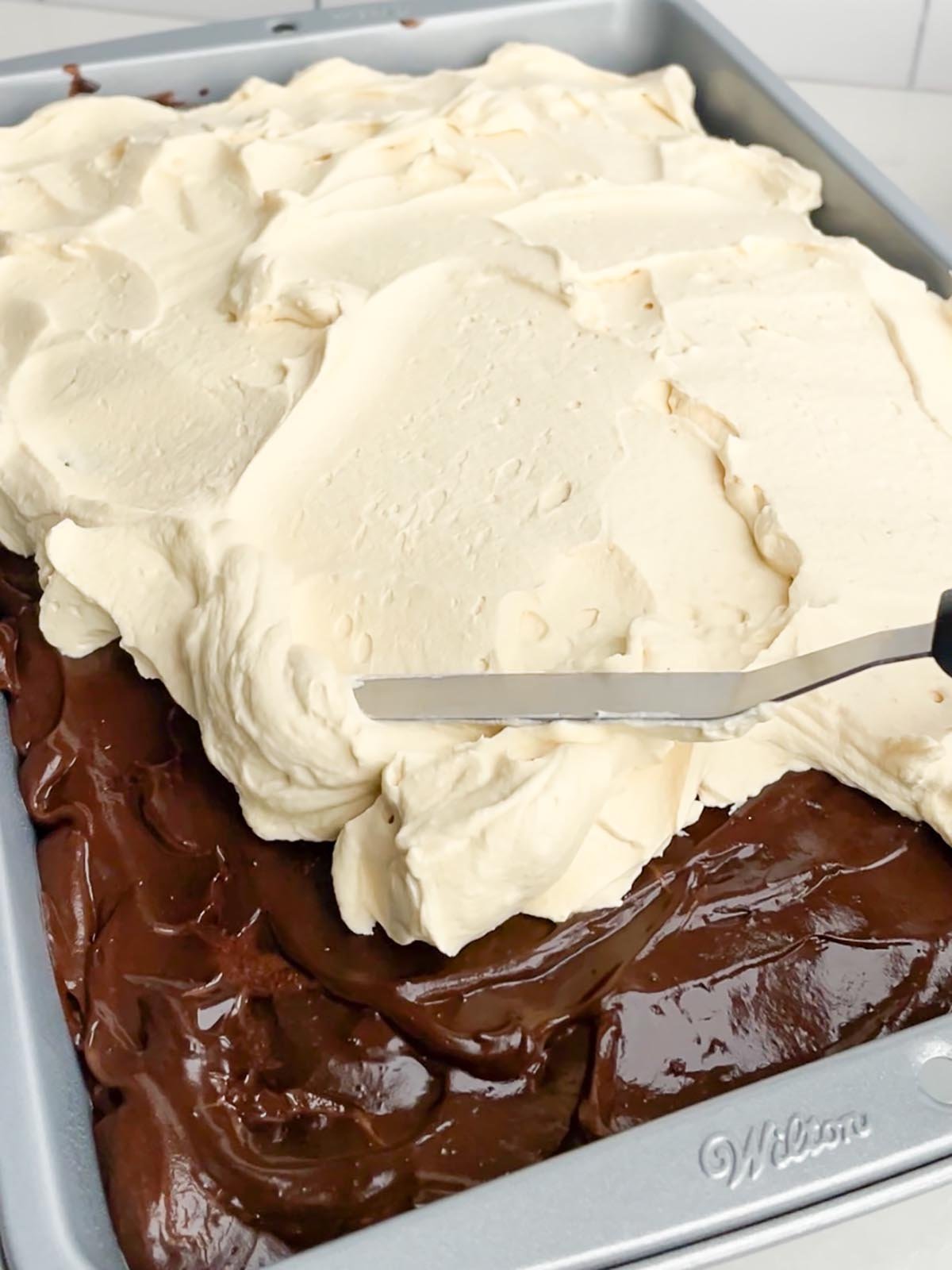 spatula spreading caramel whipped cream on a chocolate cake