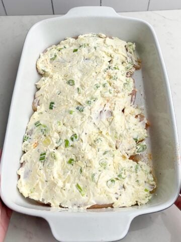 cream cheese mixture spread over chicken breasts in white baking dish.