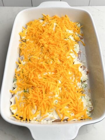 shredded cheddar cheese on top of chicken in white baking dish.