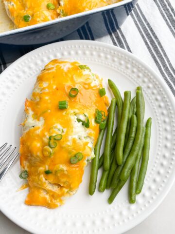 cheesy baked chicken on white plate with green beans.