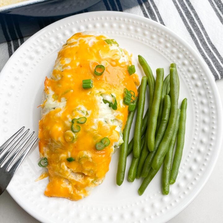 cheesy baked chicken on white plate with green beans