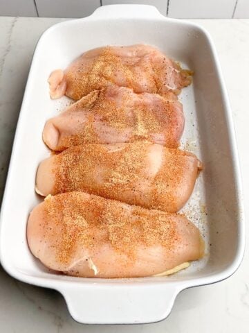 seasoned chicken breasts in white casserole dish.