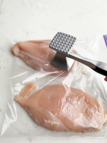 meat mallet pounding chicken in a ziptop bag.