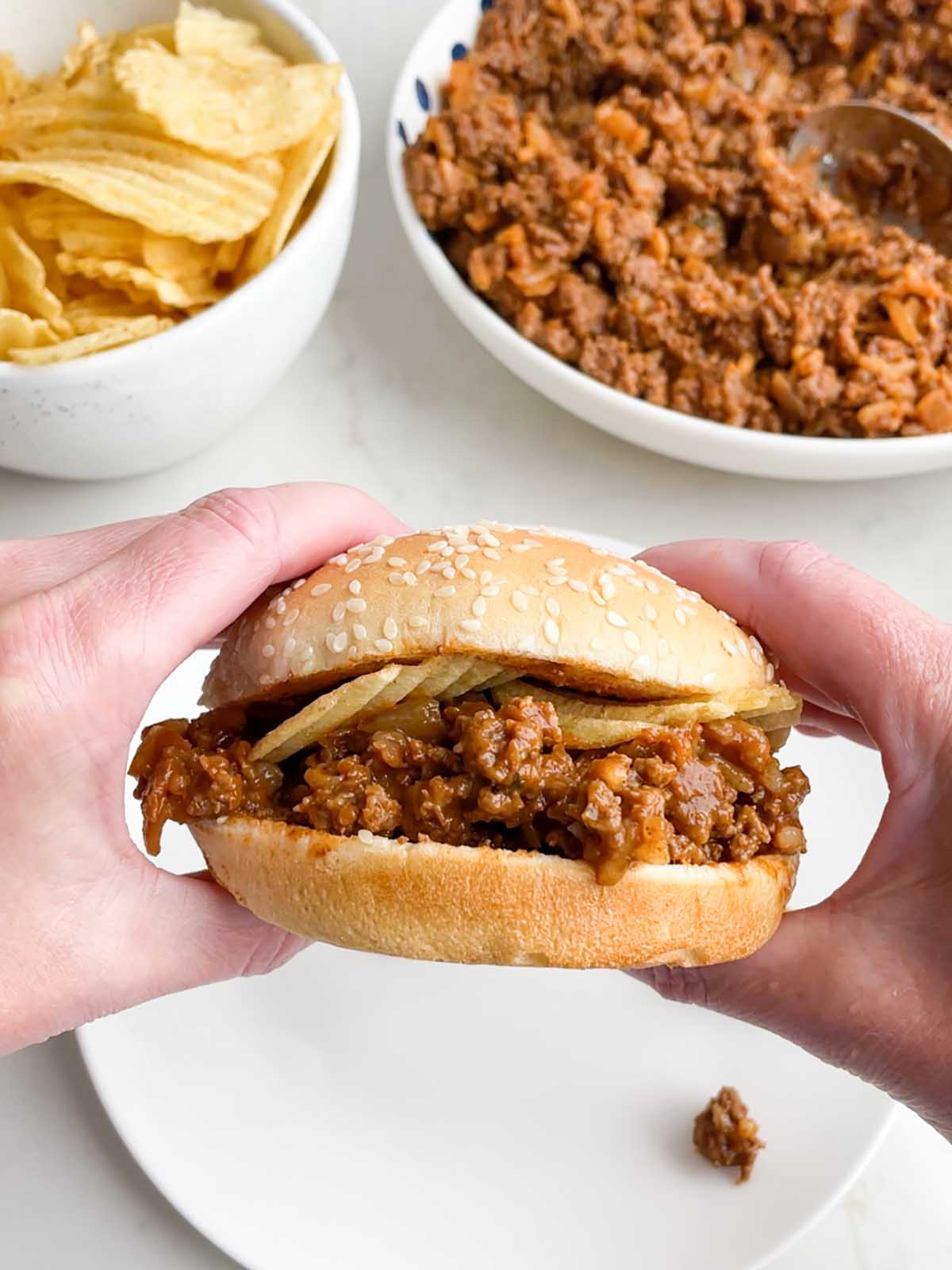 hand holding a chicken gumbo sloppy joe with potato chips