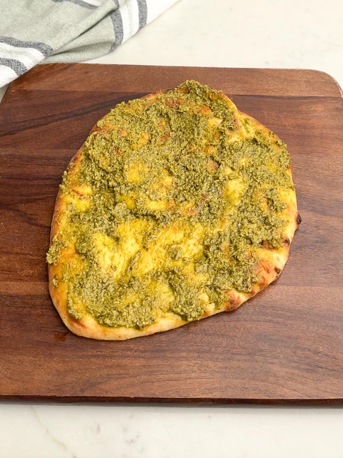 naan flatbread topped with pesto on a wooden cutting board