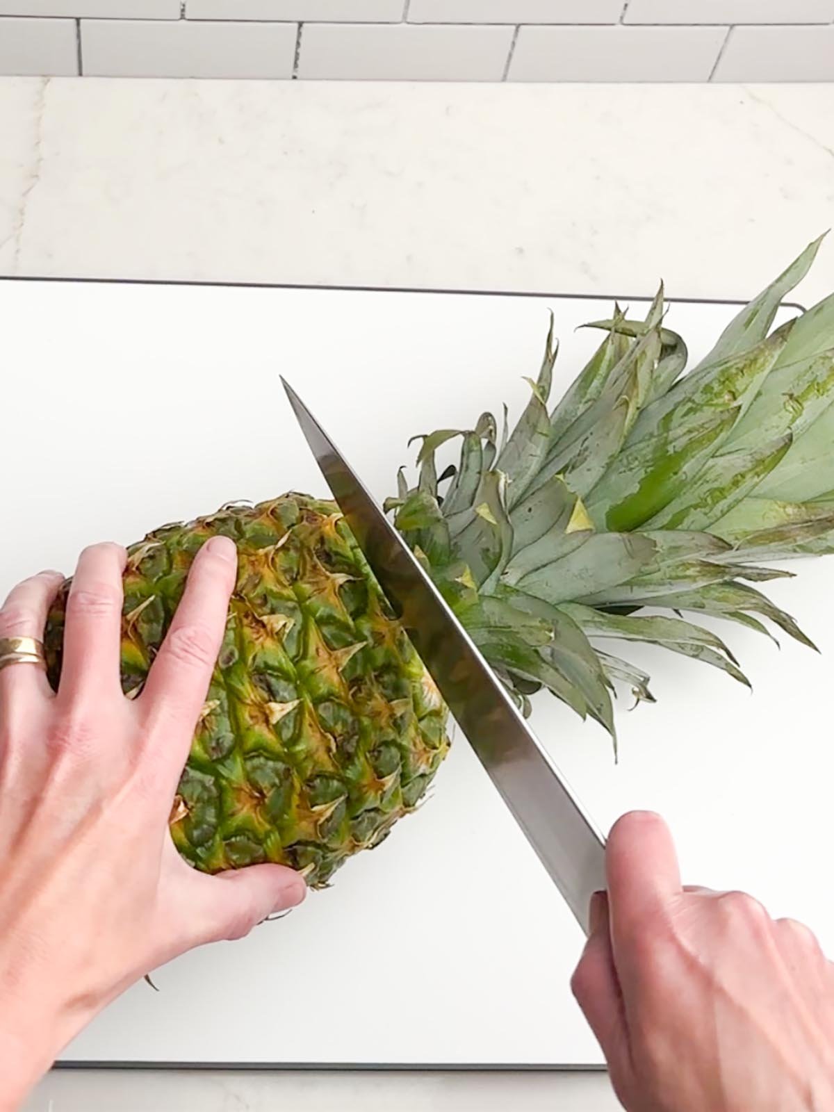 hand holding a knife slicing the top off of a pineapple
