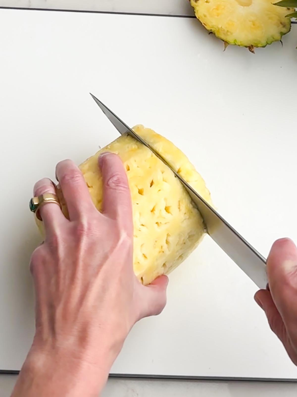 hand holding a knife cutting a pineapple into slices