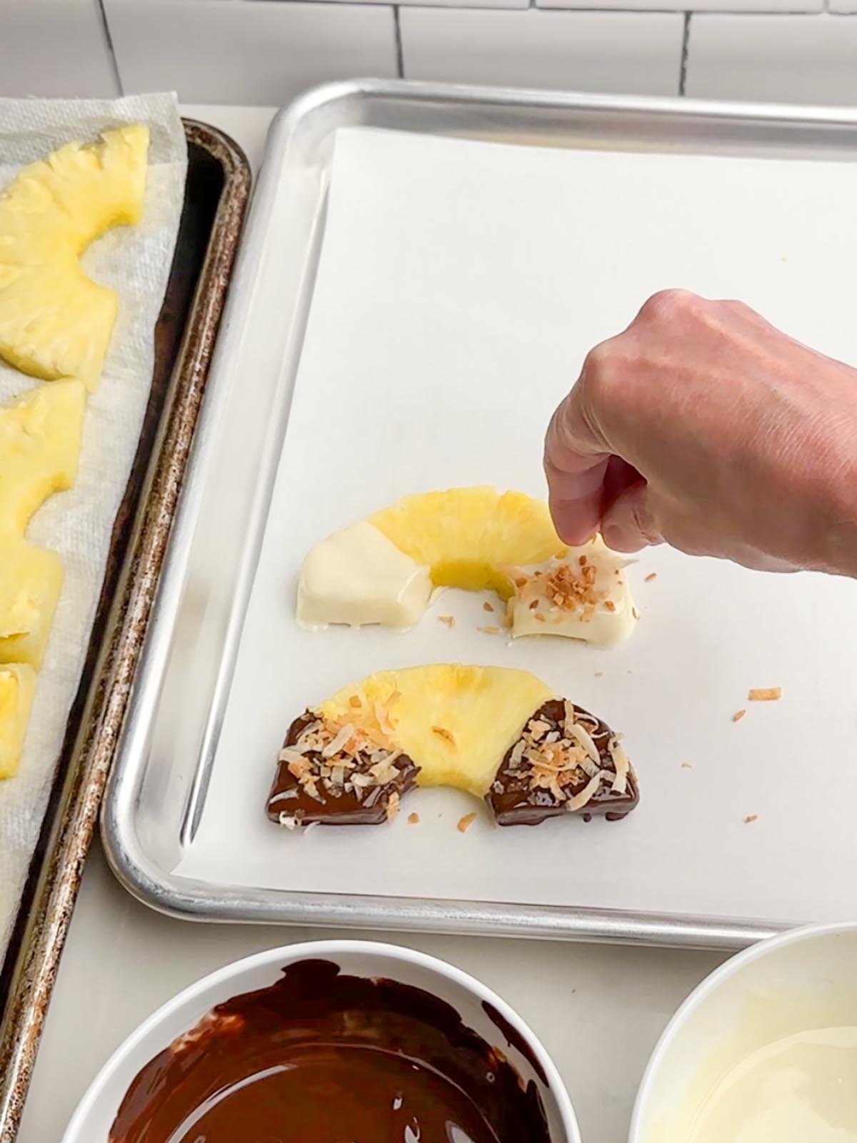 hand sprinkling toasted coconut on top of chocolate covered pineapple