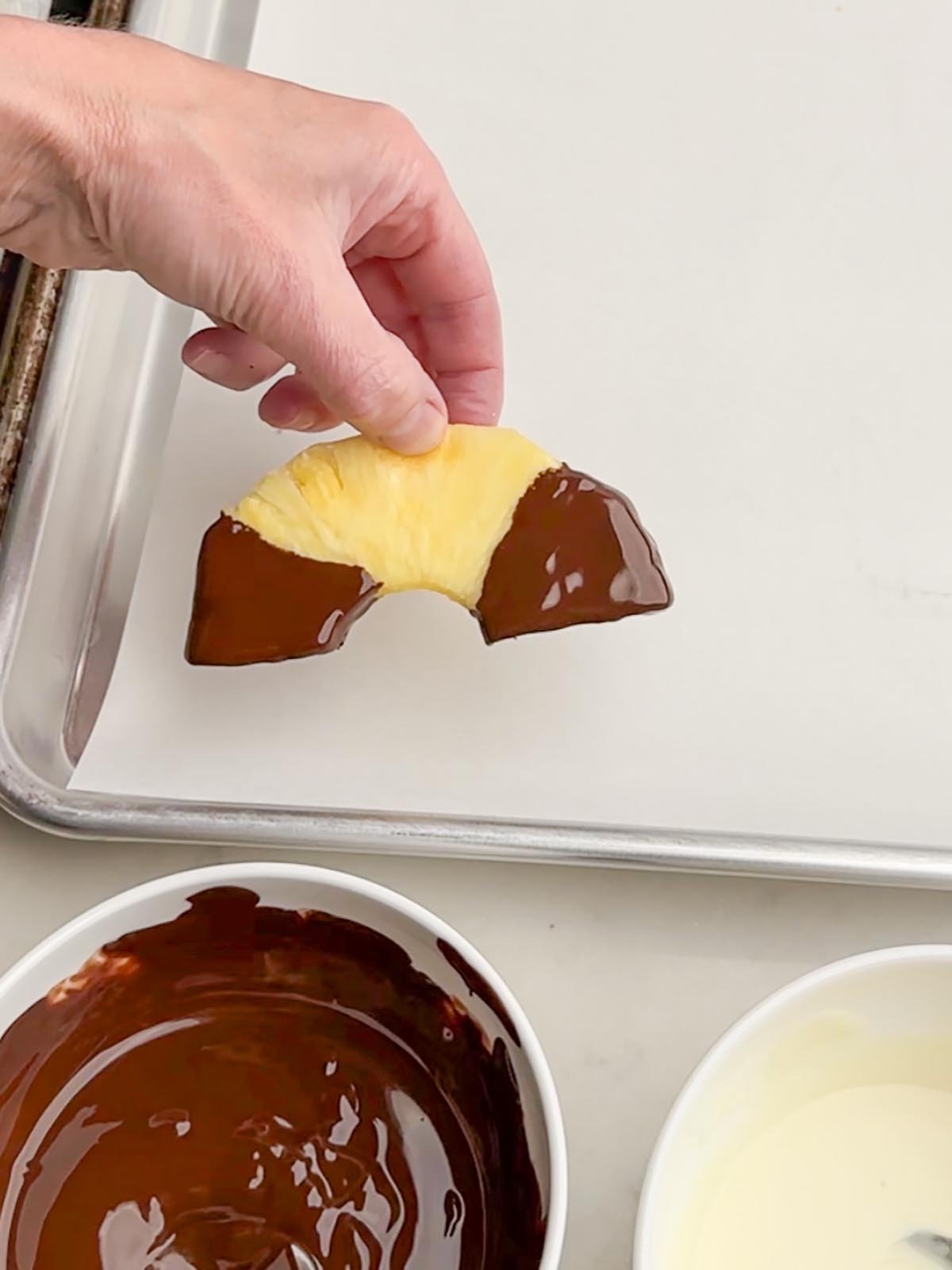 hand holding up a piece of chocolate covered pineapple