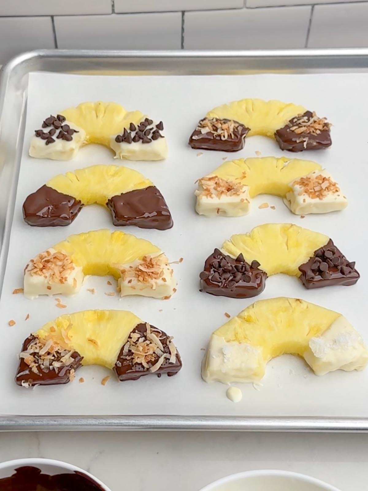 chocolate covered pineapple half rings on a parchment lined baking sheet