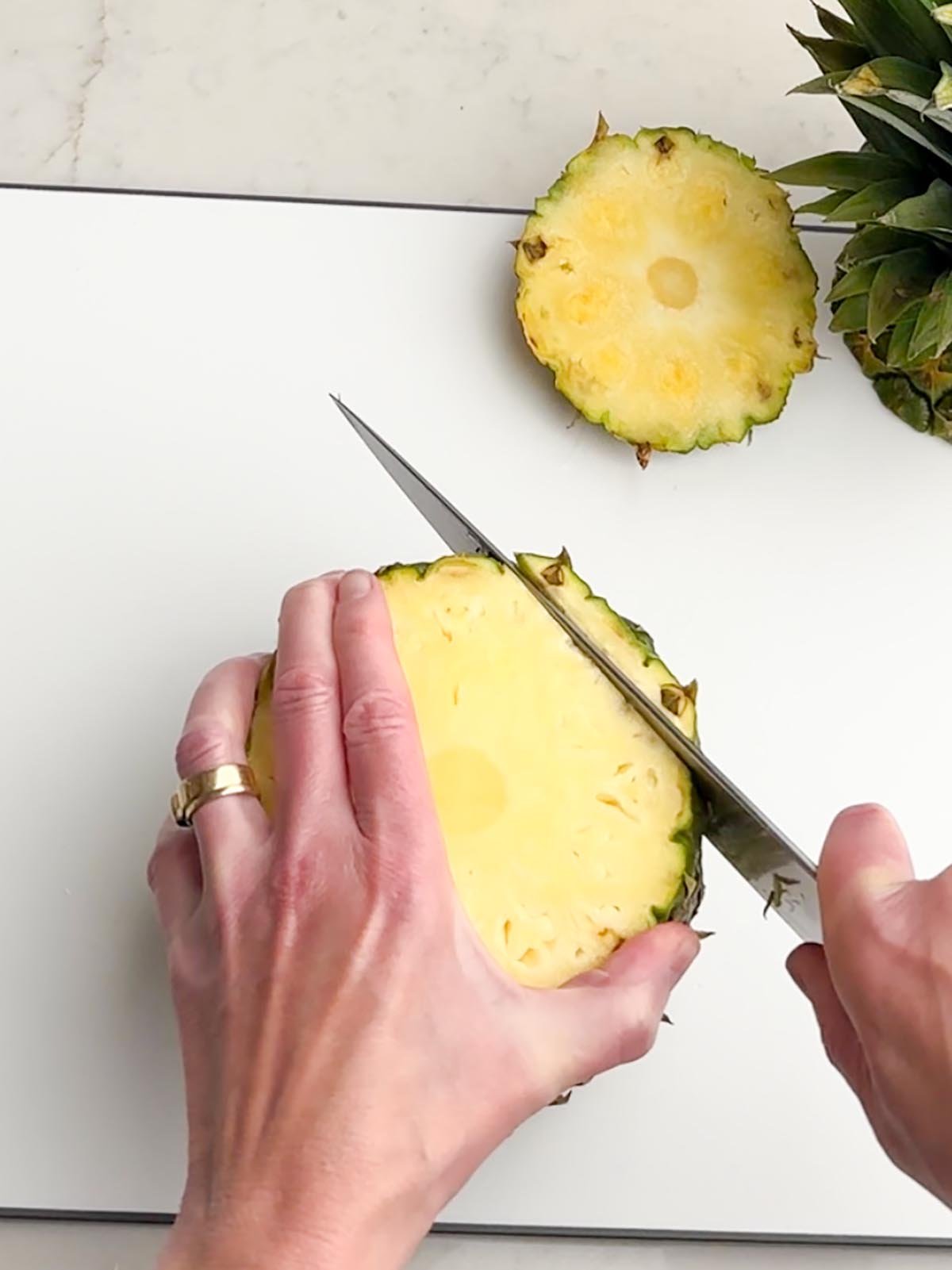 hand holding a knife slicing the rind off of a pineapple