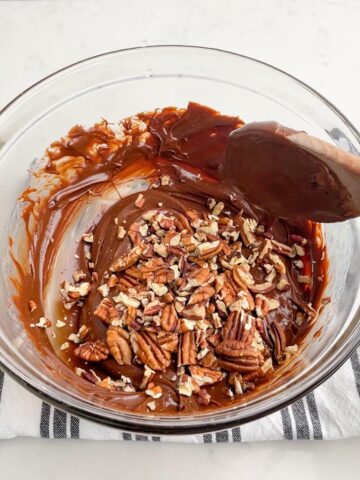 wooden spoon stirring pecans into chocolate fudge mixture.