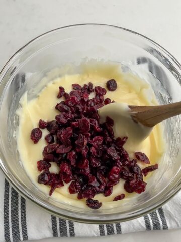 wooden spoon stirring dried cranberries into white chocolate fudge mixture.