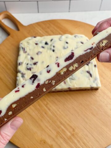 hands holding up a bar of fudge to show the white and semi sweet chocolate layers.