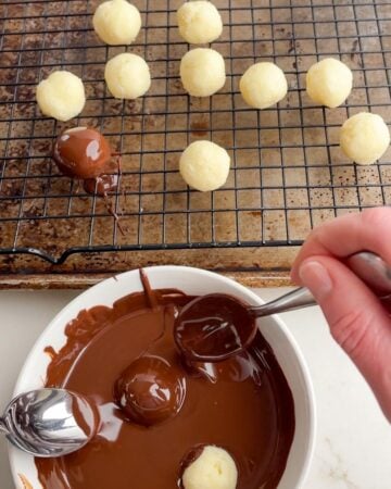 hands holding spoons dipping the coconut balls in melted chocolate. 