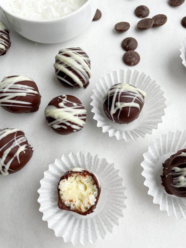 chocolate coconut balls in candy wrappers on a white countertop. 
