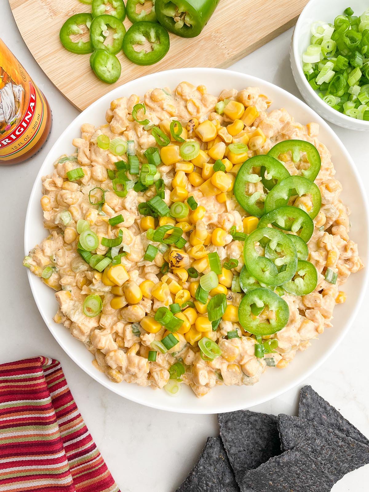 corn dip with cream cheese topped with corn, green onions, and jalapenos in a white bowl