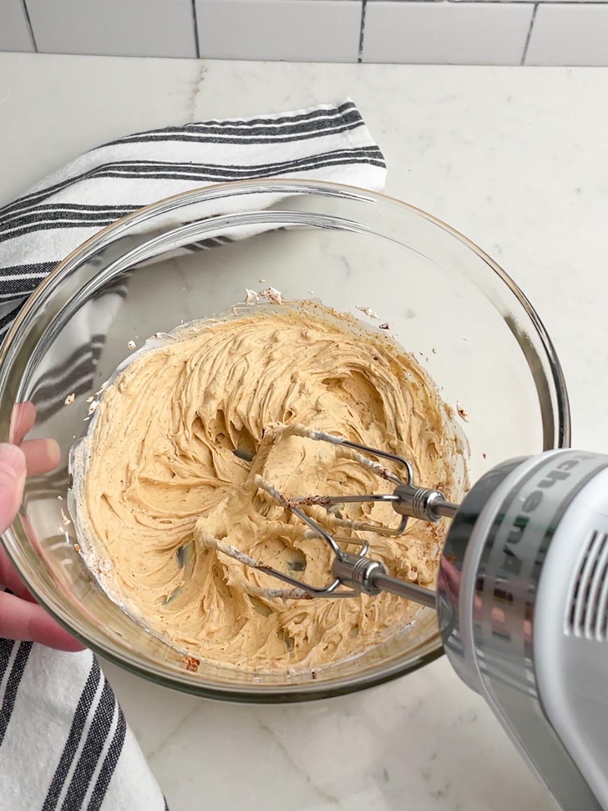 whipped cream cheese, sour cream, and spices in a clear bowl with a hand mixer