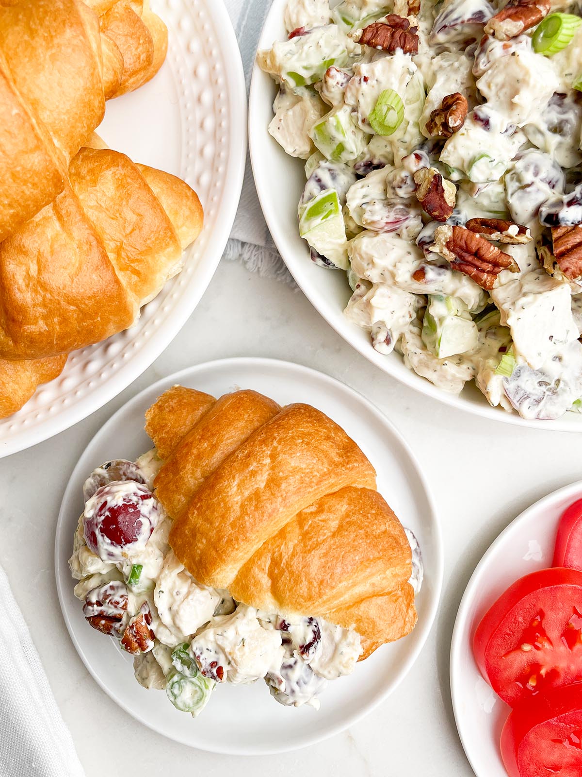 cranberry pecan chicken salad on a croissant with bowl of salad and plate of croissants in background