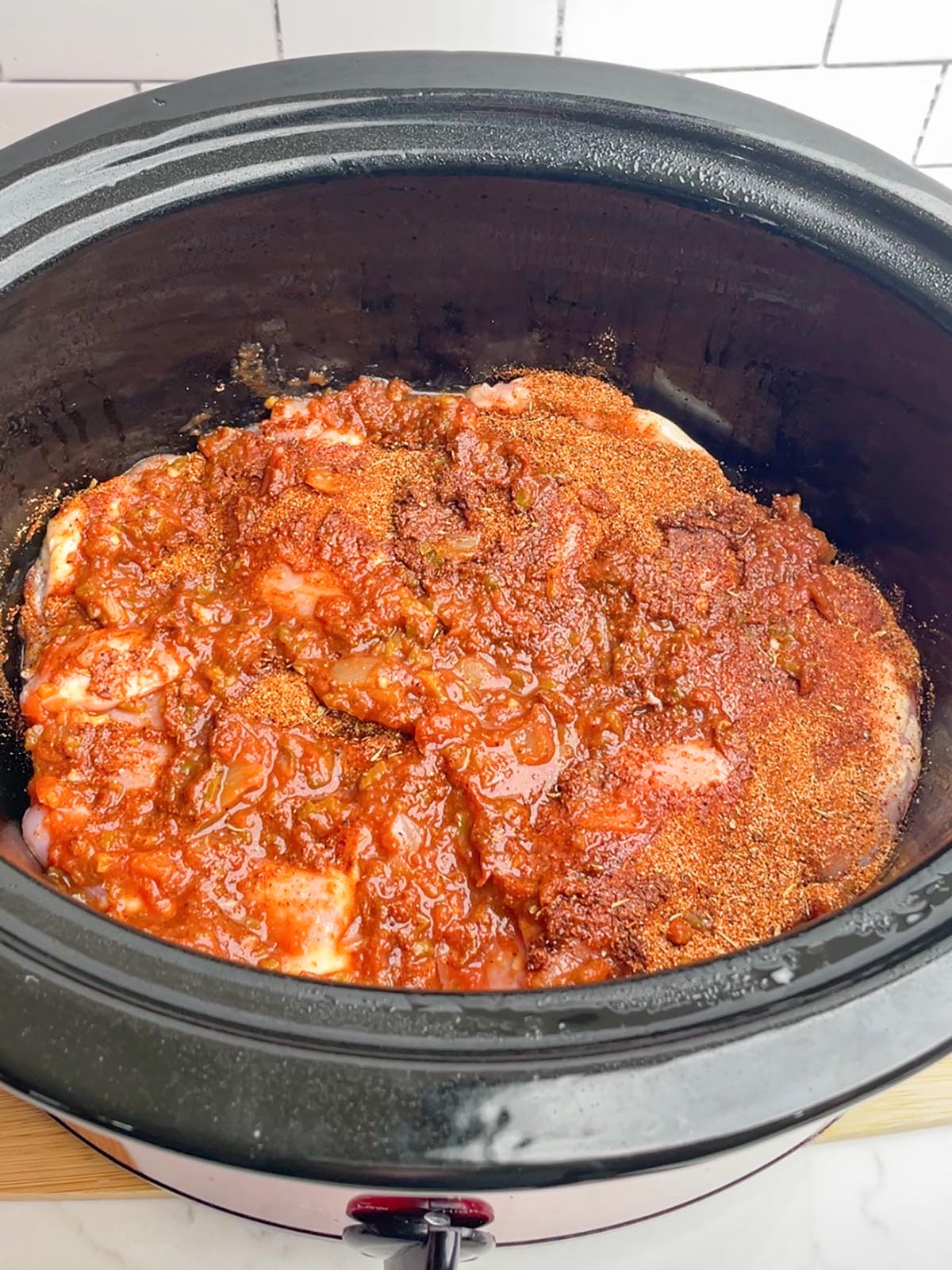 uncooked crock pot salsa chicken in black slow cooker