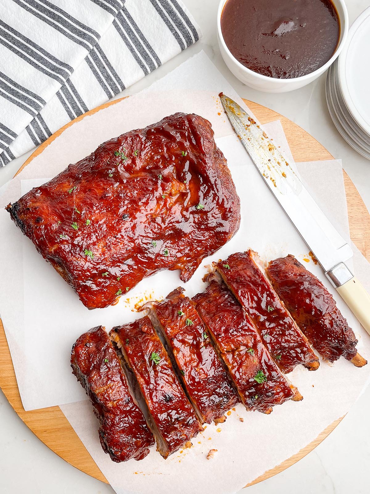 two half racks of ribs on white parchment paper on a wooden cutting board next to a knife.