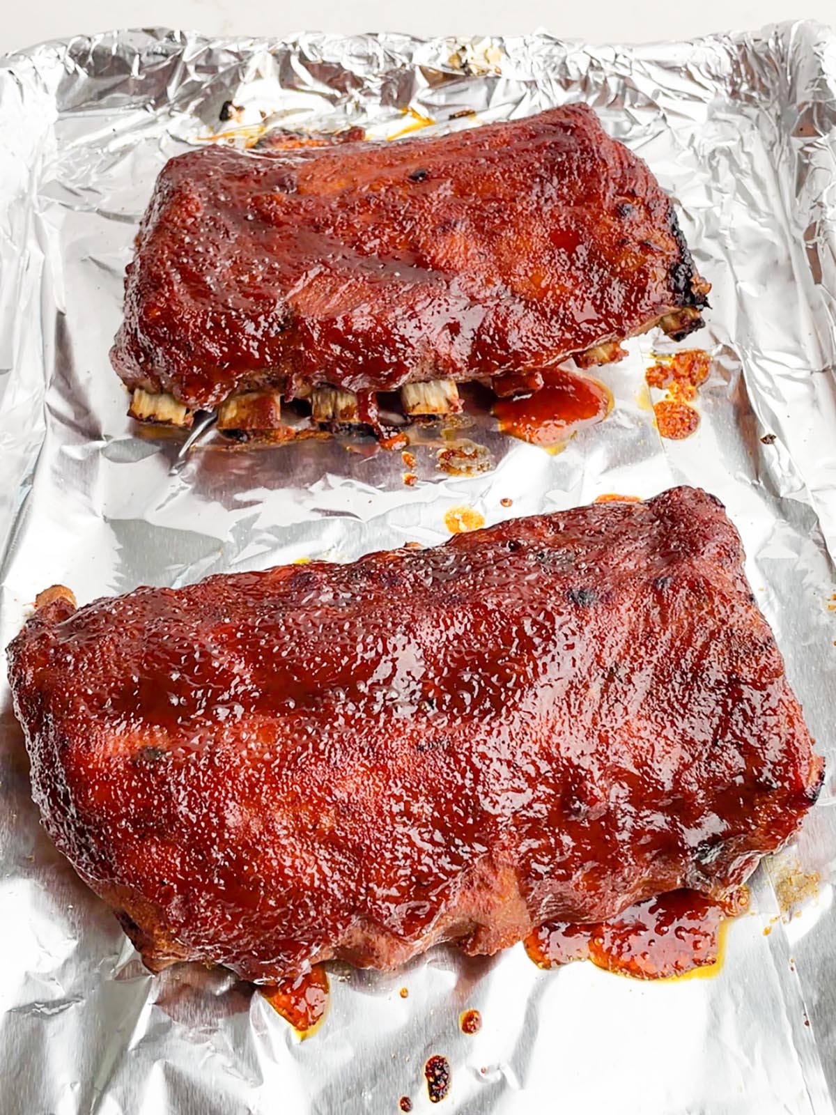 two half racks of ribs on a foil lined baking sheet.