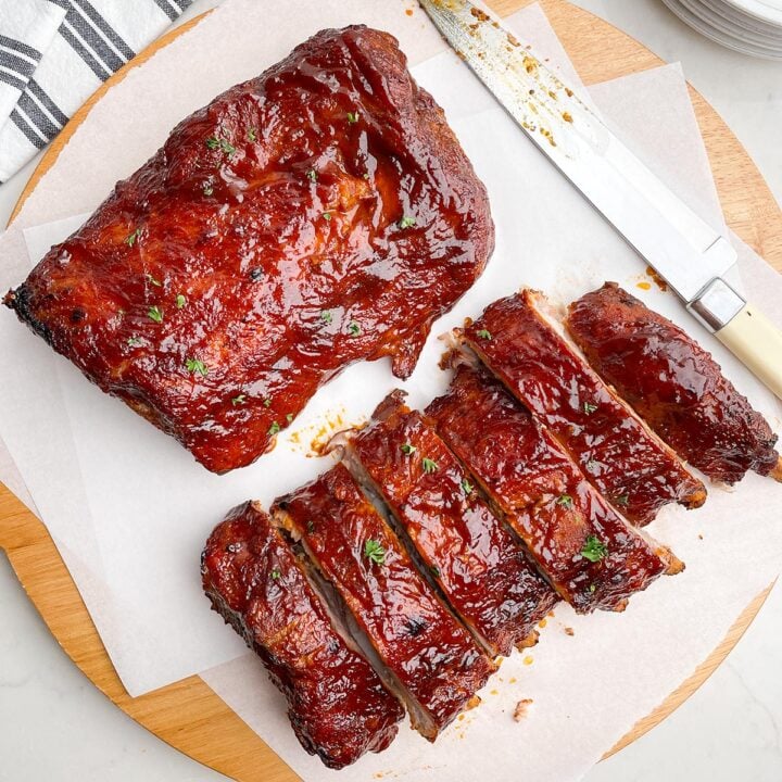 two half racks of ribs on white parchment paper on a wooden cutting board next to a knife