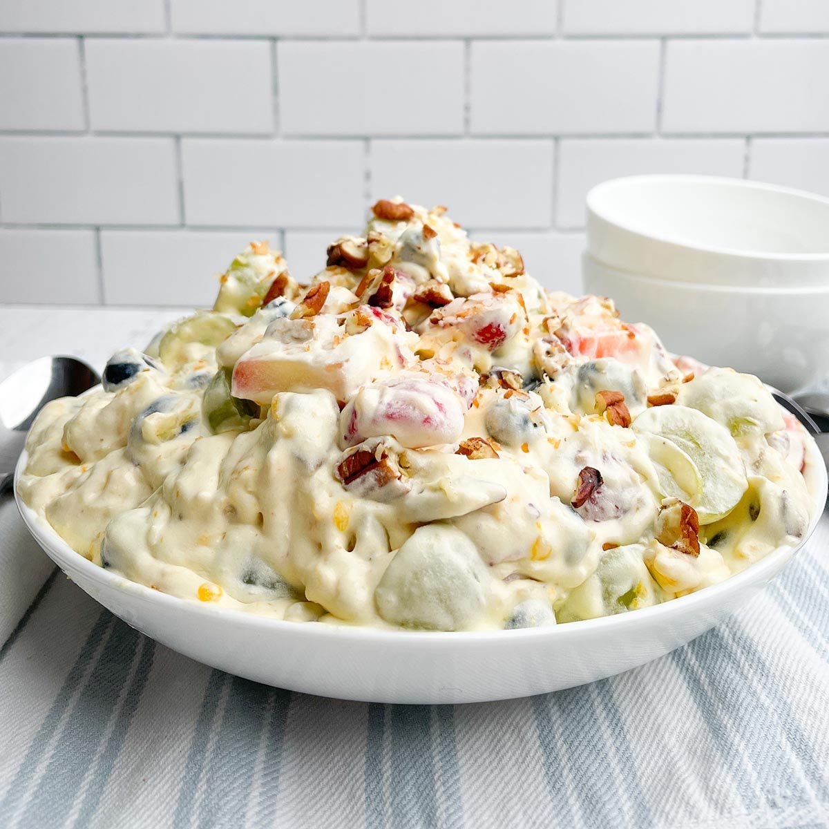 fruit salad recipe with cool whip topped with coconut and pecans in a white bowl